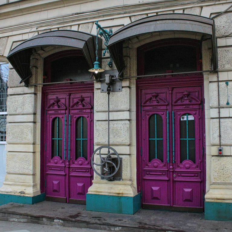 Two vibrant pink doors with ornate details and green accents, set in a stone facade.