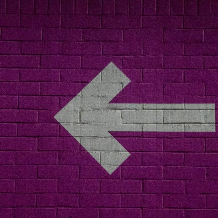 Grey left arrow on a textured purple brick wall.